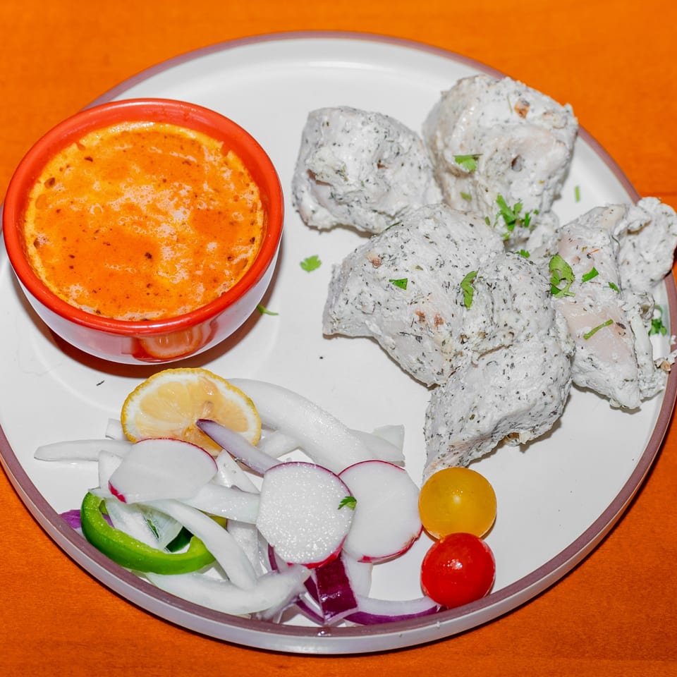 Plate of herb-seasoned chicken, creamy orange dipping sauce, lemon, radishes, onions, peppers, and cherry tomatoes.