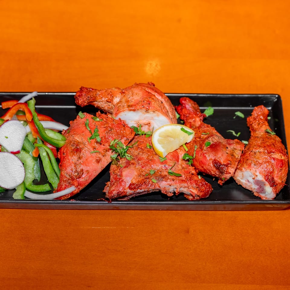 Platter of red-spiced grilled chicken garnished with cilantro and lemon, served with sliced peppers, onions, and radishes.